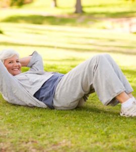 Ältere fitte Frau in Sportkleidung im Park liegt auf Wiese und macht Crunches