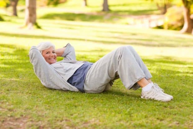 Ältere fitte Frau in Sportkleidung im Park liegt auf Wiese und macht Crunches
