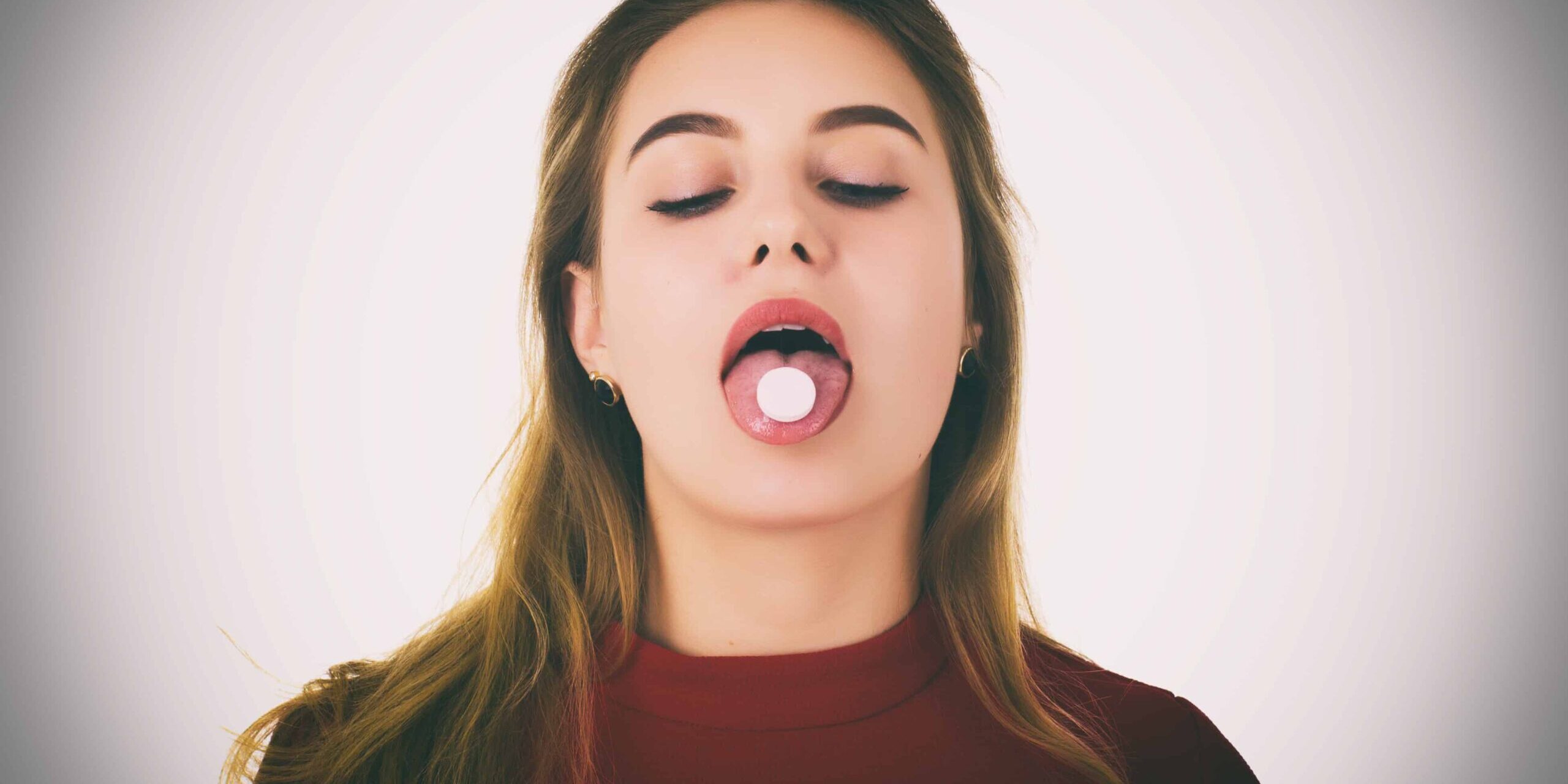 Diät Pillen Junge Frau streckt die Zunge heraus, auf der Zunge eine weiße Diät Pille