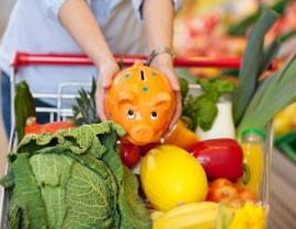 Frau legt Sparschwein in einen Einkaufswagen voller Gemüse
