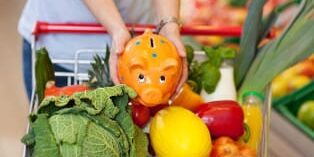 sparschwein-im-einkaufskorb_314 Frau legt Sparschwein in einen Einkaufswagen voller Gemüse