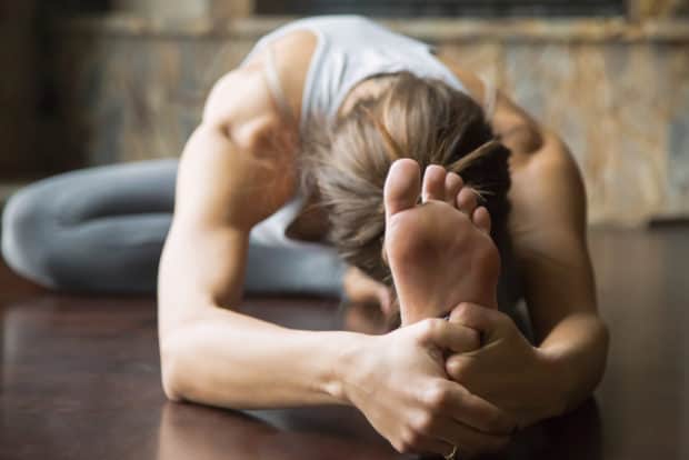 Junge Frau auf Yogamatte macht eine Vorbeuge