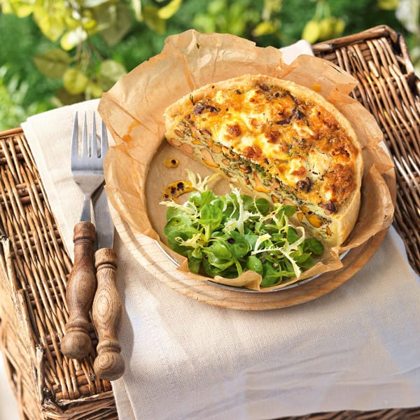 Ziegenkäsetarte auf einem Holzteller neben frische Kräutern