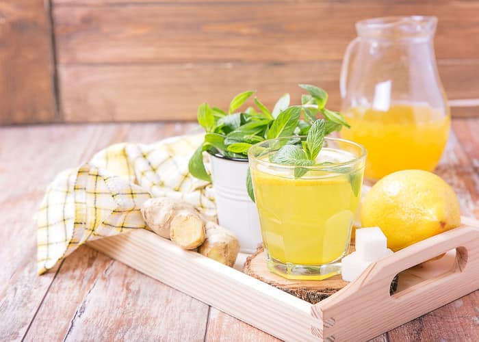 Frische Zitronenlimonade mit Minze angerichtet im Glas und der Karaffe auf einem hölzernen Tablett