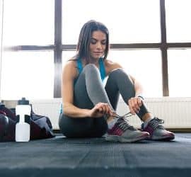 Übersäuerte Sportlerin mit Trinkflasche bindet sich die Schuhe