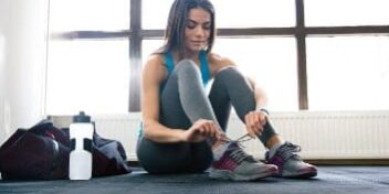 Übersäuerung_Sportlerin Übersäuerte Sportlerin mit Trinkflasche bindet sich die Schuhe